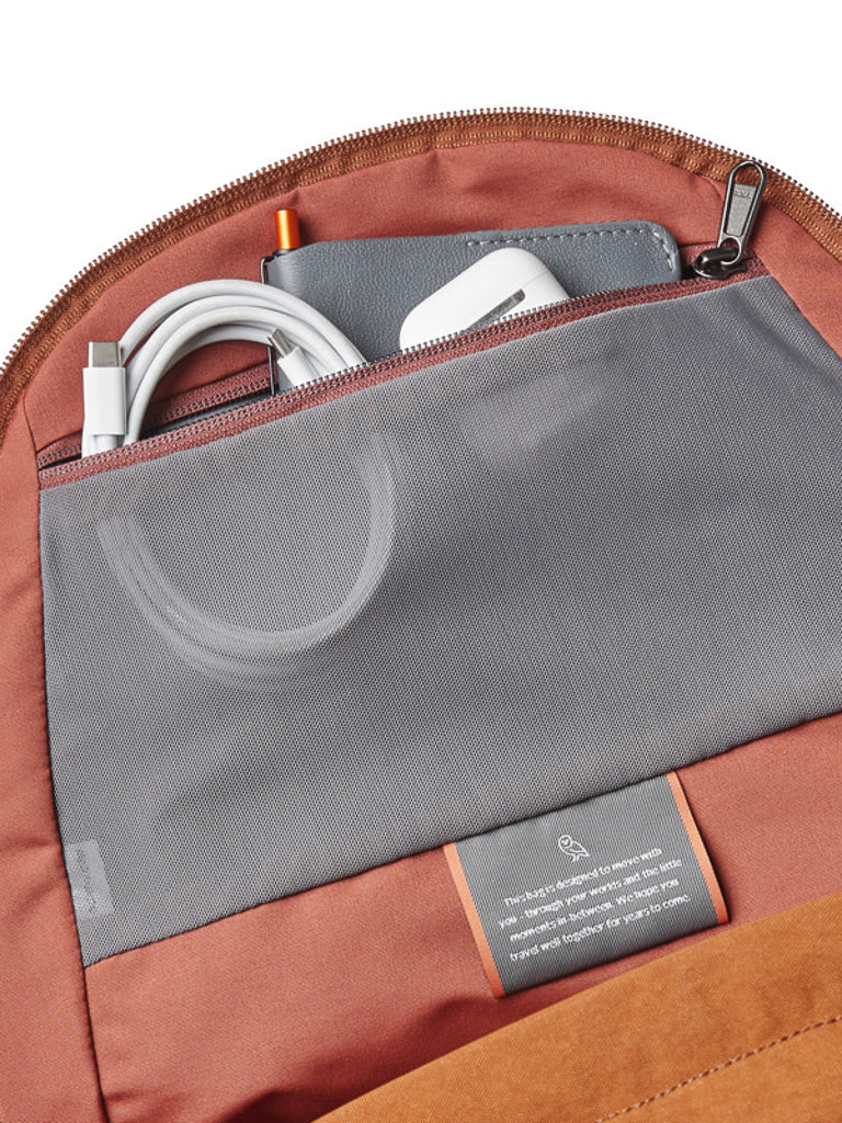 A close-up of the Bellroy Classic Backpack - 20L shows a mesh pocket storing a phone, charging cable, and white wireless earbuds. The reddish-brown lining highlights its thoughtful design with recycled materials.