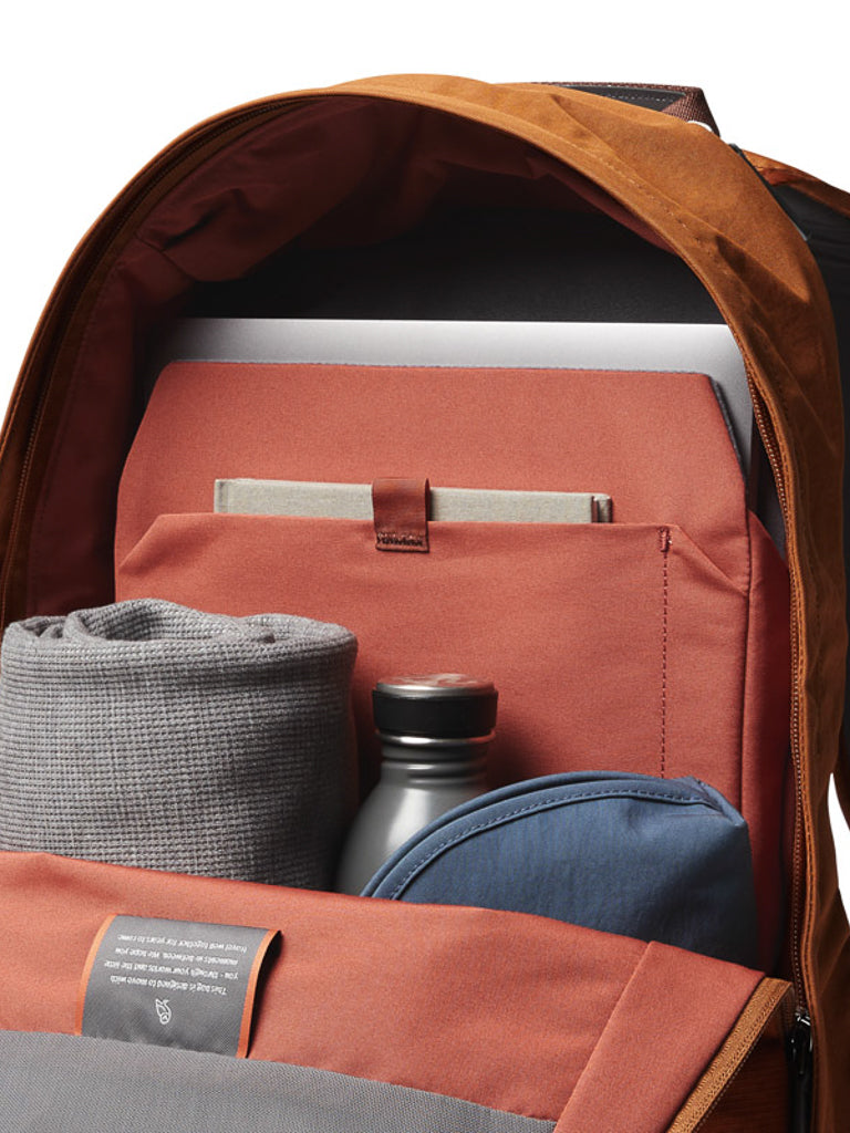 The Bellroy Classic Backpack - 20L reveals a rolled gray fabric, black water bottle, closed blue pouch, red folder, laptop, and notebook—neatly organized inside this stylish bag made from recycled materials.