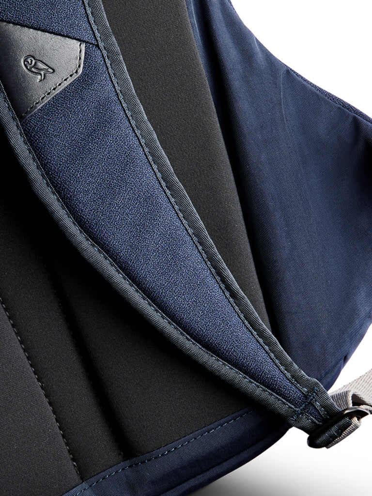Close-up of the Bellroy Classic Backpack - 20L in navy blue and black, highlighting its water-resistant textured material, precise stitching, a pocket corner, and part of a metal buckle or strap on the right.