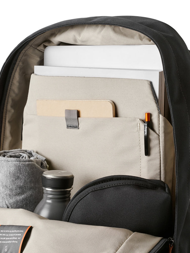The Bellroy Classic Backpack - 20L displays organized essentials—a notebook, pencil, rolled gray fabric, water bottle, and folders—each neatly stored in separate compartments crafted from recycled materials.