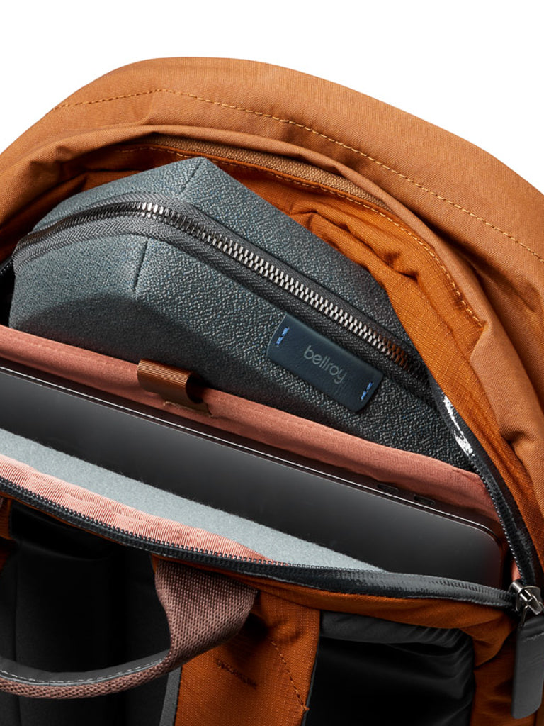 Close-up of an open rust-colored Bellroy Classic Backpack Plus - 24L made from water-resistant recycled fabric, with a gray Bellroy pouch and a laptop organized in separate compartments.