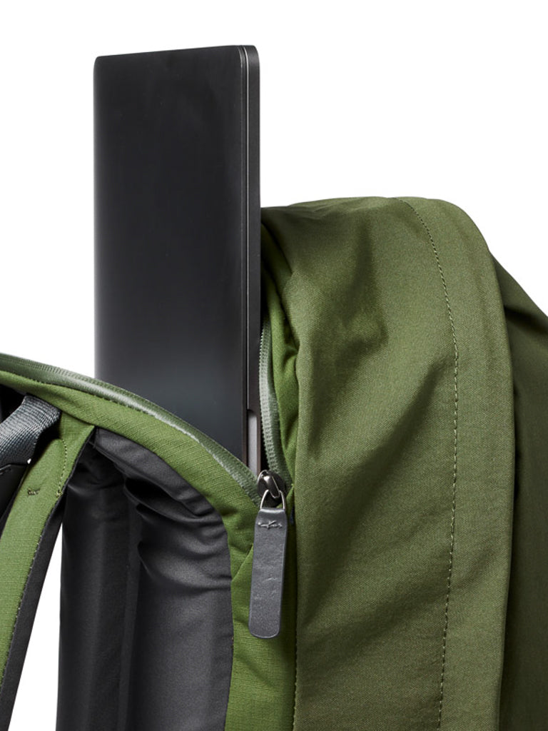 A close-up of the Bellroy Classic Backpack Plus - 24L in green, crafted from water-resistant recycled fabric, shows a black laptop being placed into or removed from its padded compartment through the partially open zipper.
