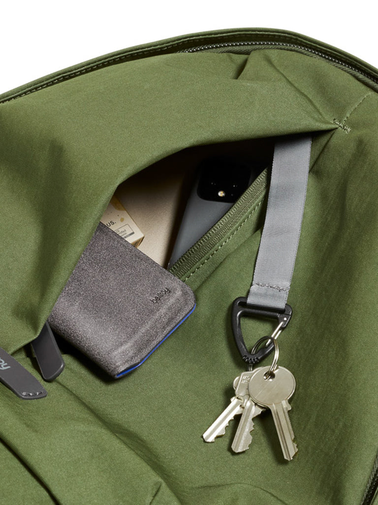 Close-up of the Bellroy Classic Backpack Plus - 24L dual compartment pocket, crafted from water-resistant recycled fabric, holding a gray wallet, smartphone, papers, and a gray strap with three metal keys attached.