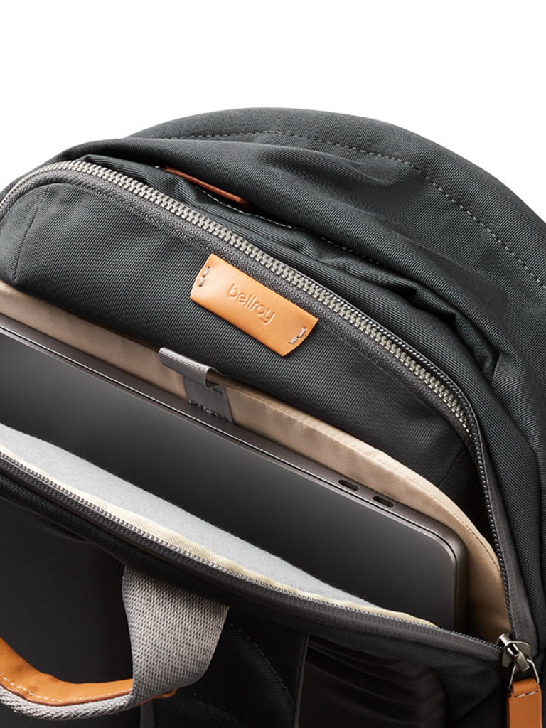 A close-up of the Bellroy Classic Backpack Plus - 24L in black shows its dual compartments with tan leather zipper pulls, neatly storing a laptop and tablet in padded sleeves, all made from water-resistant recycled fabric.