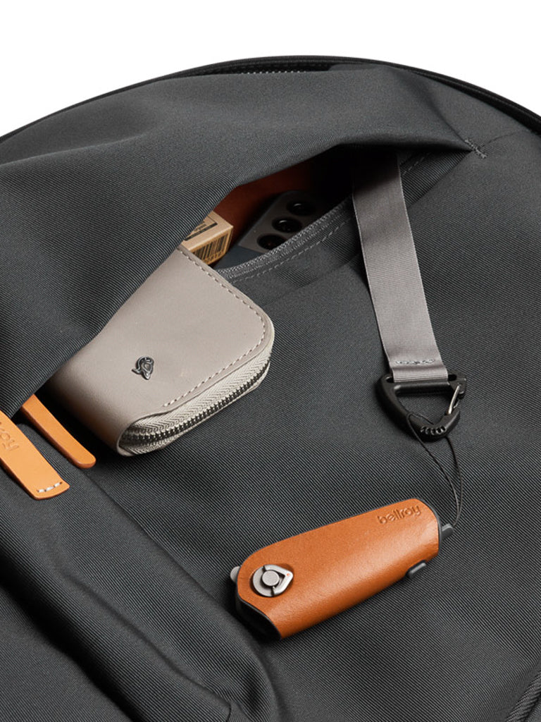 A close-up of the Bellroy Classic Backpack Plus - 24L’s outer pocket, partially open to show a beige wallet, cards, and a tan leather key holder with a grey strap. Crafted from water-resistant recycled fabric for daily durability.