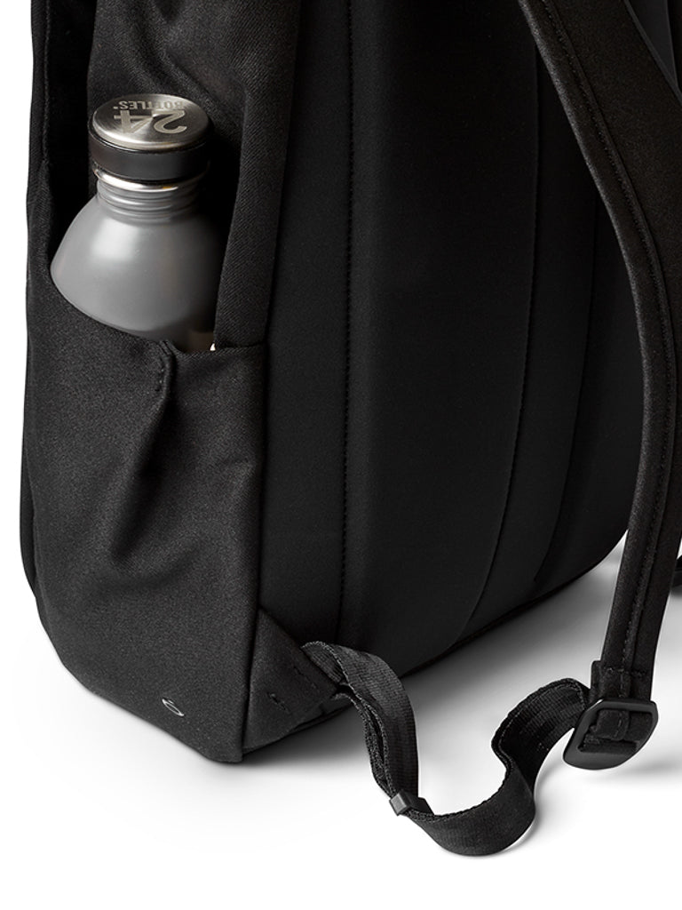 A close-up of Bellroy’s Melbourne Backpack Compact 13L shows its side pocket holding a gray metal water bottle, with part of the strap and bottom corner also visible against a white background.