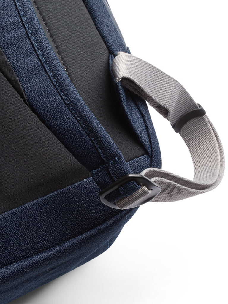 Close-up of the Bellroy Melbourne Backpack Compact 13L's navy blue corner, showcasing a grey adjustable strap with a black plastic buckle on a white background.