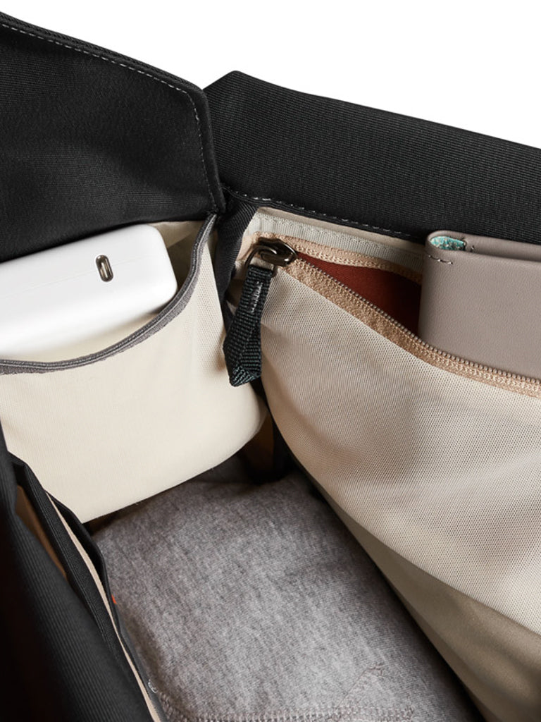 Close-up of the Bellroy Melbourne Backpack Compact 13L interior, showing a white device in a pocket and a gray wallet or phone in a zippered compartment, with gray fabric lining at the bottom.