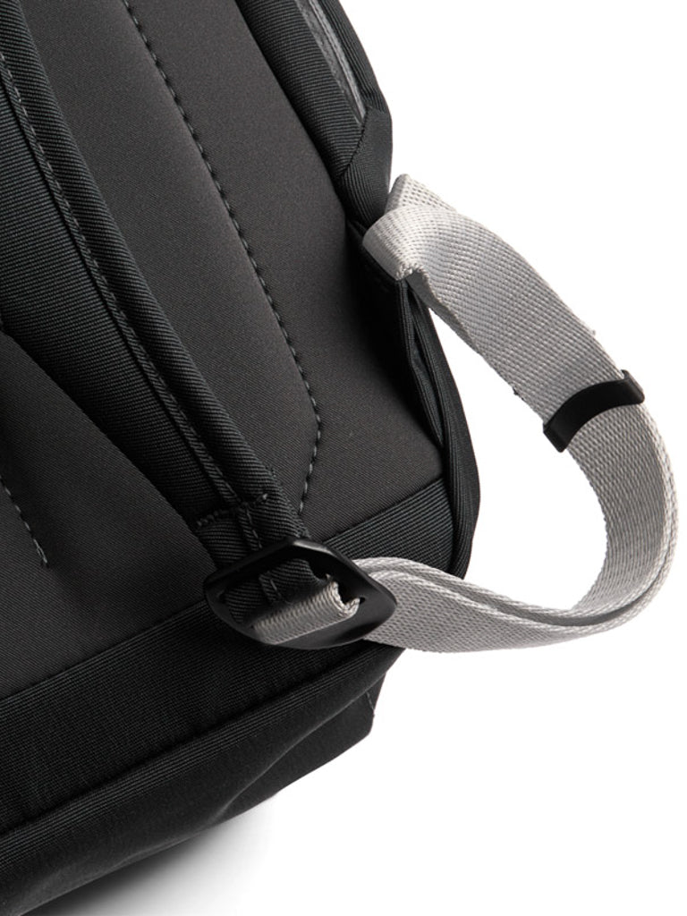 Close-up of the Bellroy Melbourne Backpack Compact 13L in black, highlighting its minimalist design, detailed stitching, and a gray strap with a black plastic buckle on the top corner.
