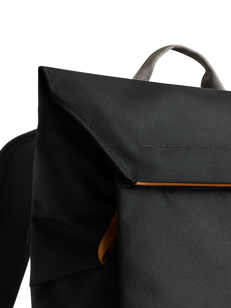 Close-up of the upper part of the Bellroy Melbourne Backpack Compact 13L, featuring a modern black minimalist design, fold-over flap, light gray handle, and a touch of orange lining at the edge.