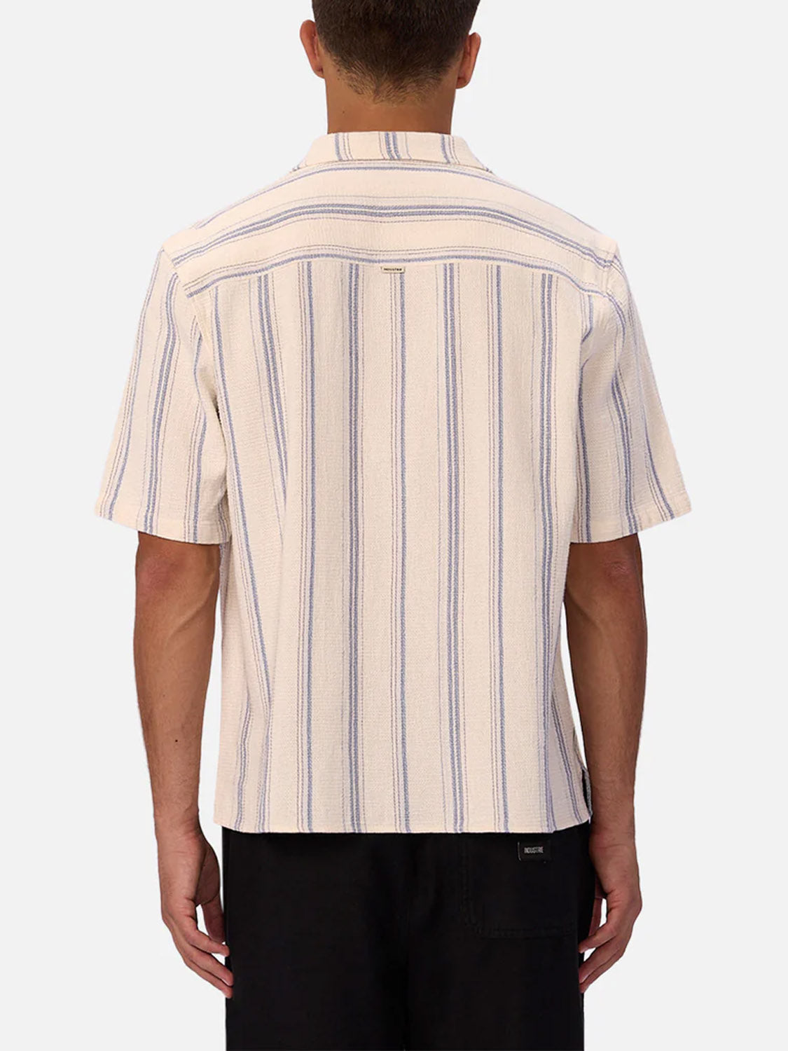 A man is shown from the back wearing the Industrie Bowment Short Sleeve Shirt with vertical blue stripes and black pants, set against a plain light background.