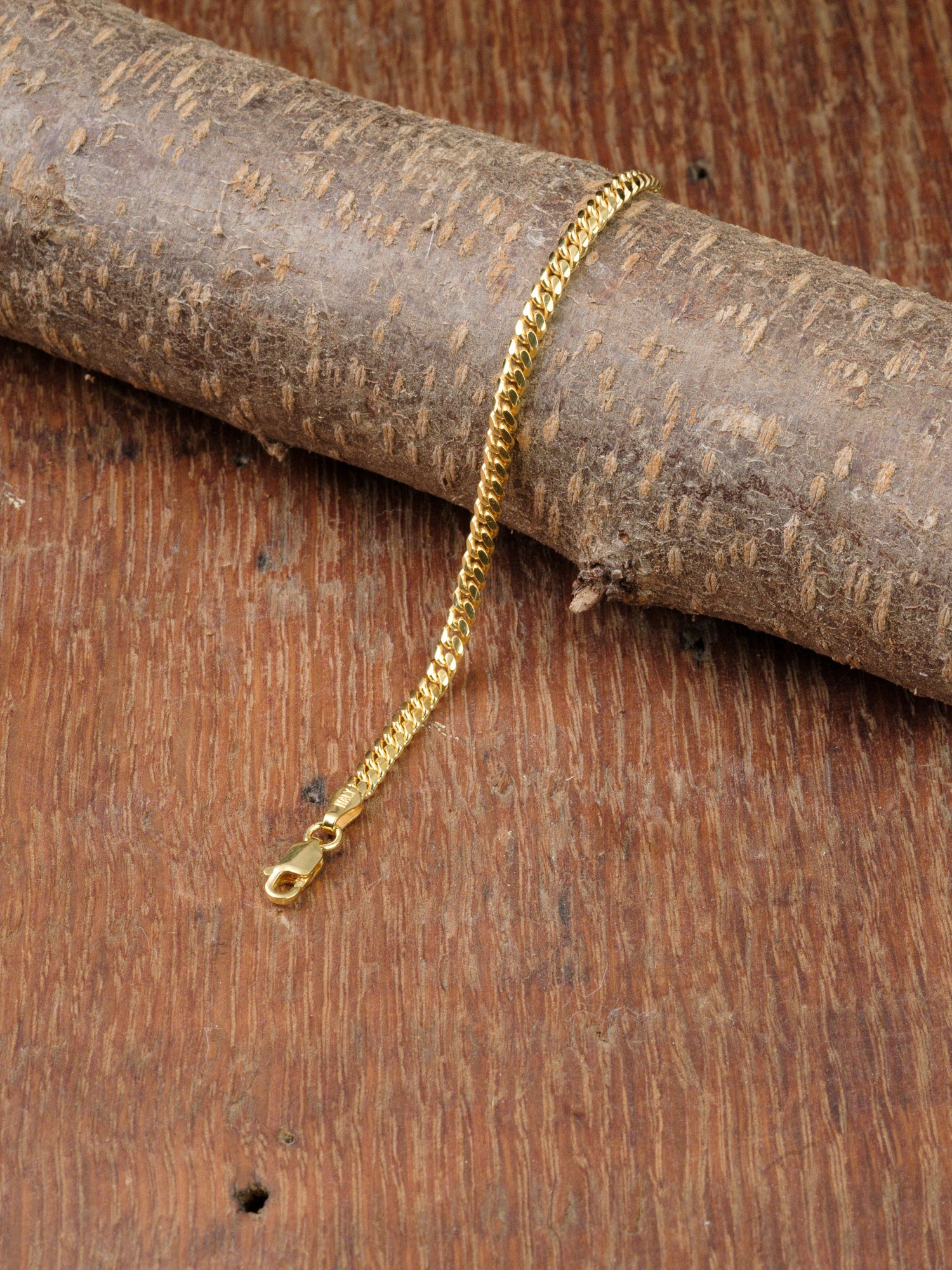 The Blaze 100 Miami Cuban Bracelet by ID Menswear, featuring a lobster clasp, is draped over a textured wooden log on a wooden surface.