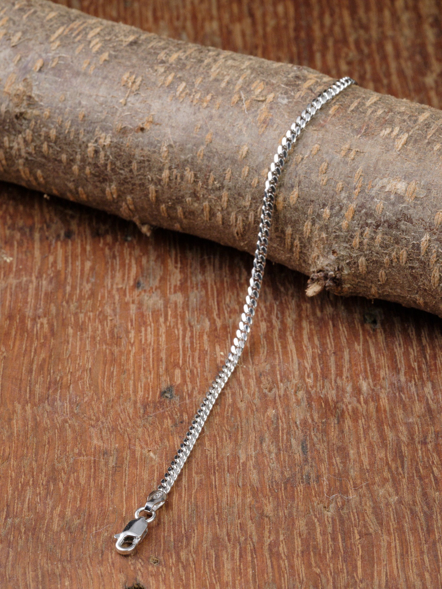 The Blaze 80 Miami Cuban Bracelet by ID Menswear, featuring a silver finish and lobster clasp, is shown on a textured wooden surface with part of the chain draped over a thick tree branch.