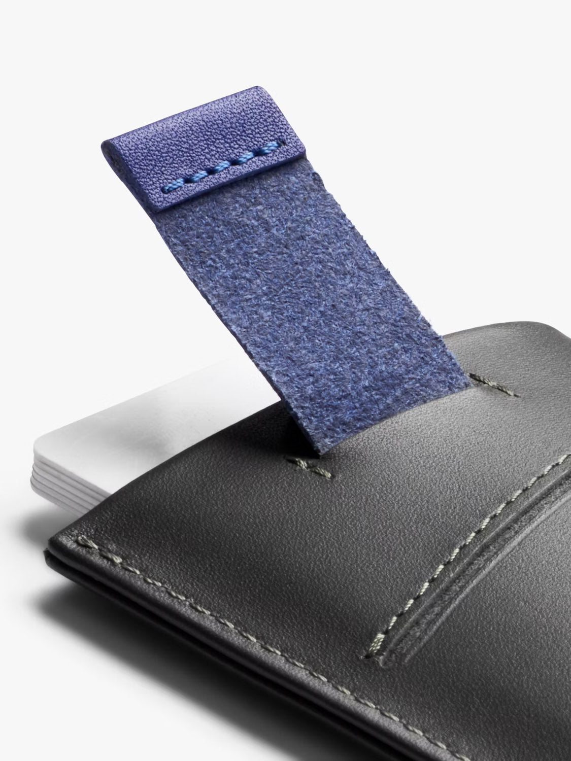 Close-up of the Bellroy Card Sleeve Wallet in black leather with visible stitching, showcasing a partially extended blue fabric pull tab and a stack of white cards inside.