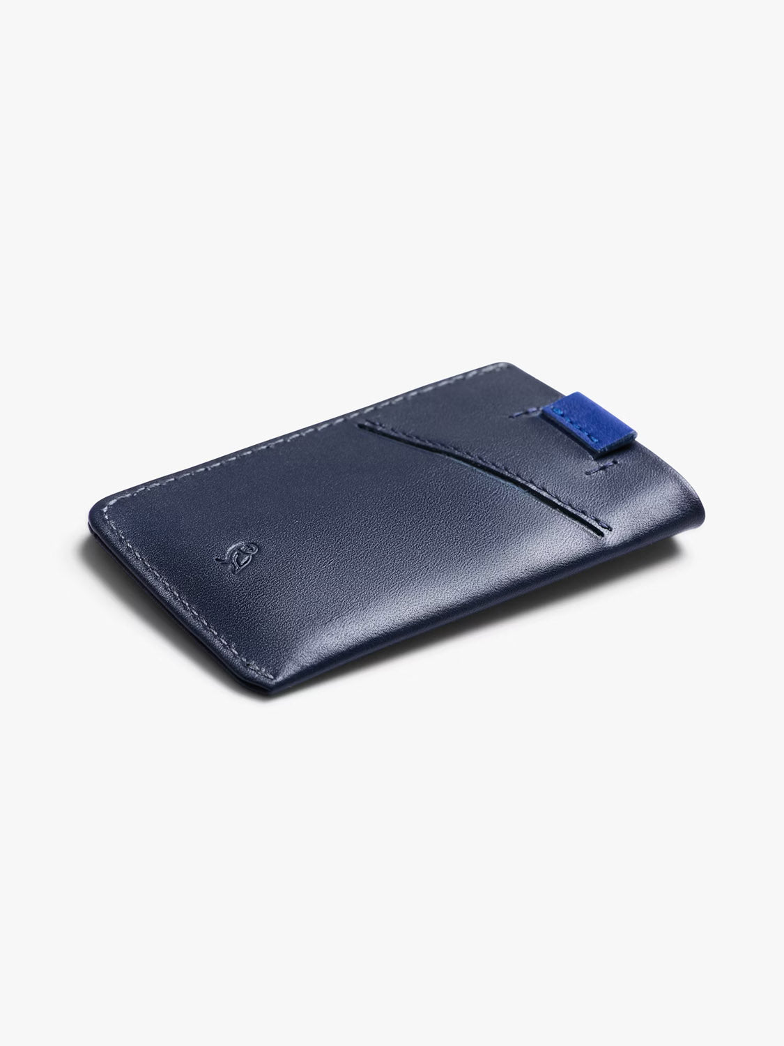 The Bellroy Card Sleeve Wallet is a slim, navy blue premium leather card holder with a single front pocket and a small blue fabric tab, shown on a plain white background.