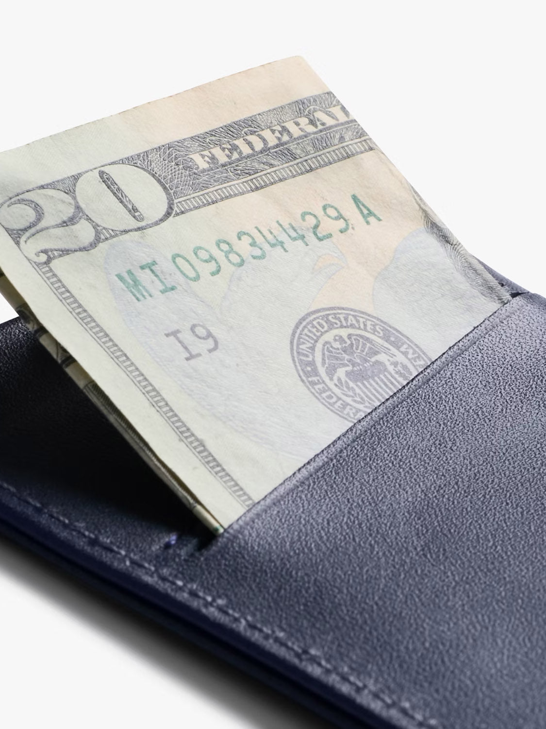 A close-up of a twenty-dollar bill partially sticking out of a dark blue Bellroy Card Sleeve Wallet against a white background.