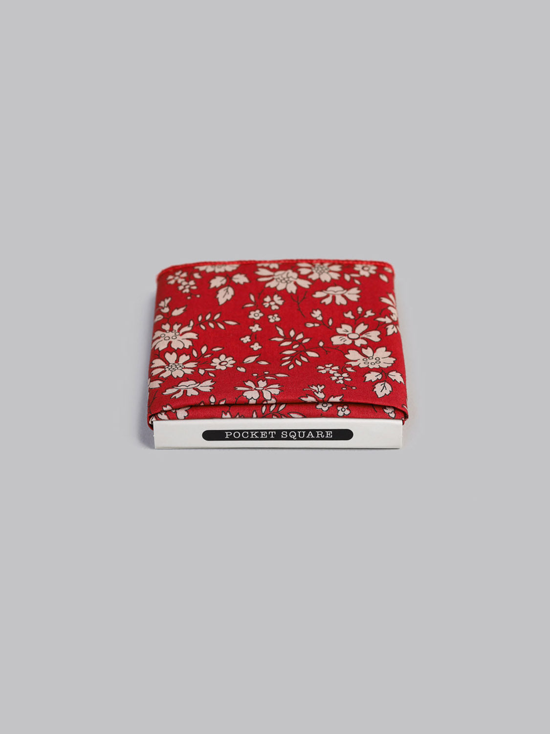 The ID Menswear Liberty™ Carpel Pocket Square, made from Tana Lawn cotton in red with a white floral print, is neatly folded and partially tucked in white packaging marked POCKET SQUARE against a plain light gray background.