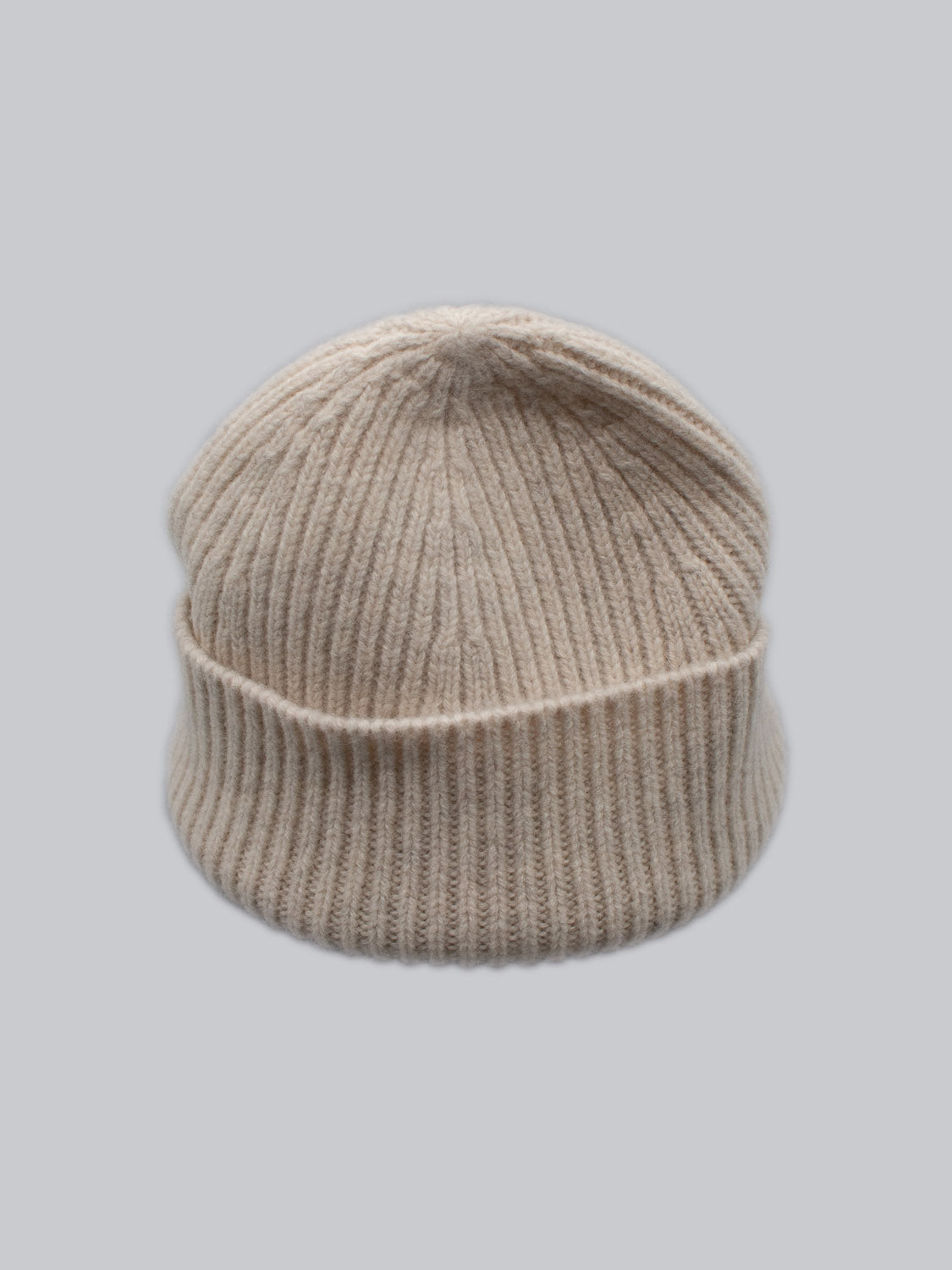 The ID Menswear Chamonix Wool Beanie, crafted from 100% wool, is showcased on a light gray backdrop. Its beige ribbed knit and folded brim provide stylish natural insulation to keep you warm.