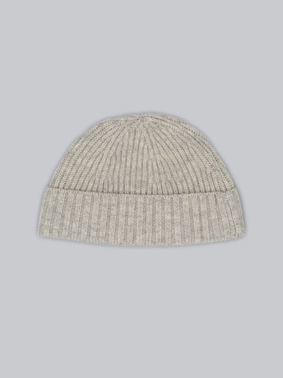 A light gray Cho Oyu Merino Wool Fishermans Beanie by ID Menswear, featuring a cozy ribbed texture and folded brim, is centered against a pale blue background.