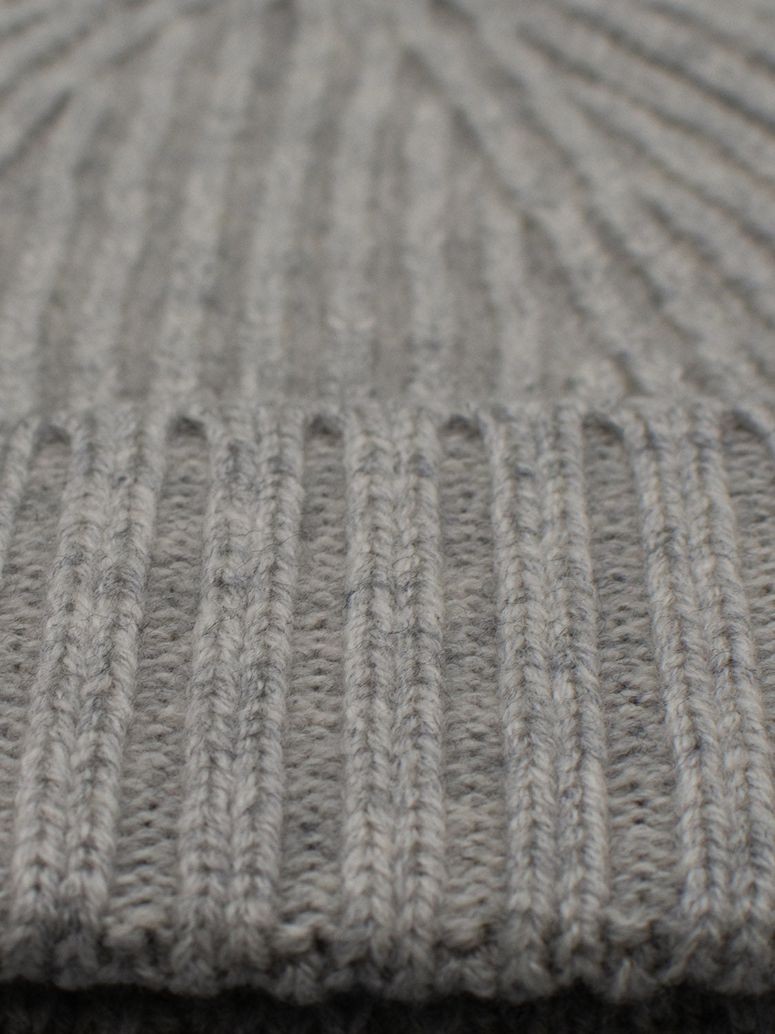 Close-up of ID Menswear’s Cho Oyu Merino Wool Fishermans Beanie, featuring a gray knitted fabric with vertical ribbed texture. Its blend of thick and thin lines gives it a soft, cozy look—ideal for winter.