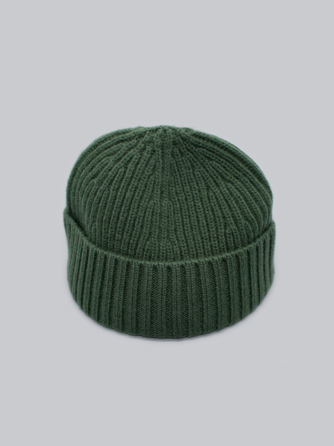 Meet the Cho Oyu Merino Wool Fishermans Beanie by ID Menswear, a winter wardrobe must-have. This green beanie is crafted from soft merino wool and features a ribbed pattern with a folded brim, all elegantly set against a light grey background.