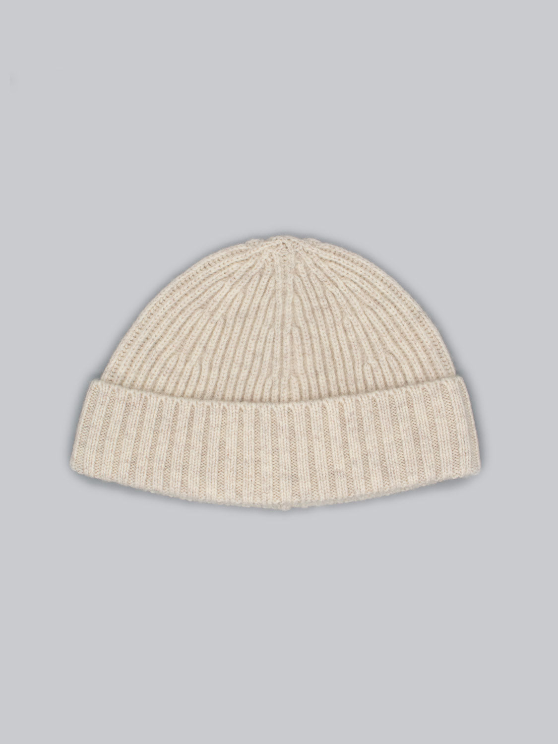 The Cho Oyu Merino Wool Fishermans Beanie by ID Menswear is a cream-colored, ribbed knit beanie with a folded brim, set against a light gray background—ideal for enhancing your winter style.