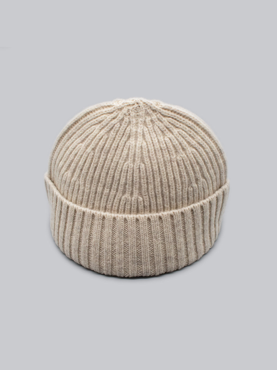 The Cho Oyu Merino Wool Fishermans Beanie by ID Menswear, featured on a light gray background, is beige with a ribbed texture and folded brim. Made from soft merino wool, this cozy accessory is perfect for your winter wardrobe.