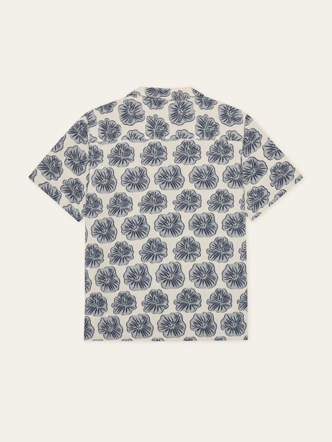 The Les Deux Dahlia Jacquard SS Shirt features a navy blue hibiscus pattern on a white background, displayed from the back against an off-white backdrop.