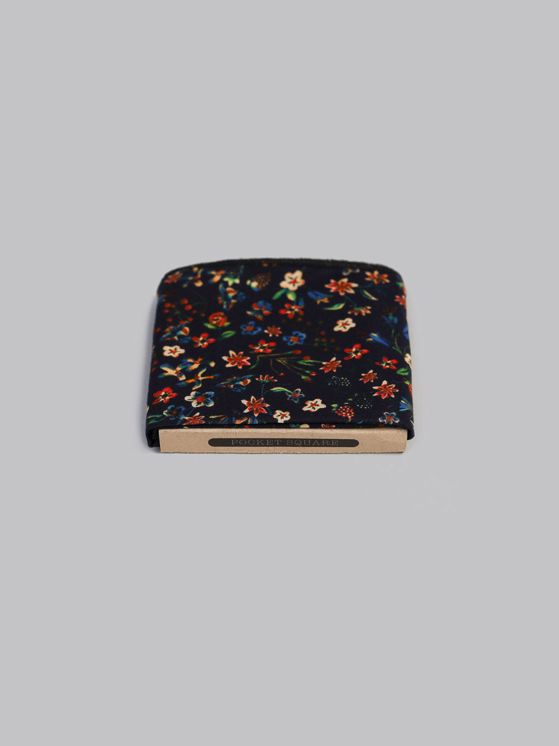A Liberty™ Donna Pocket Square by ID Menswear, featuring a colorful floral pattern, rests on a gray surface partially atop a brown box labeled HORSE & SQUAD.