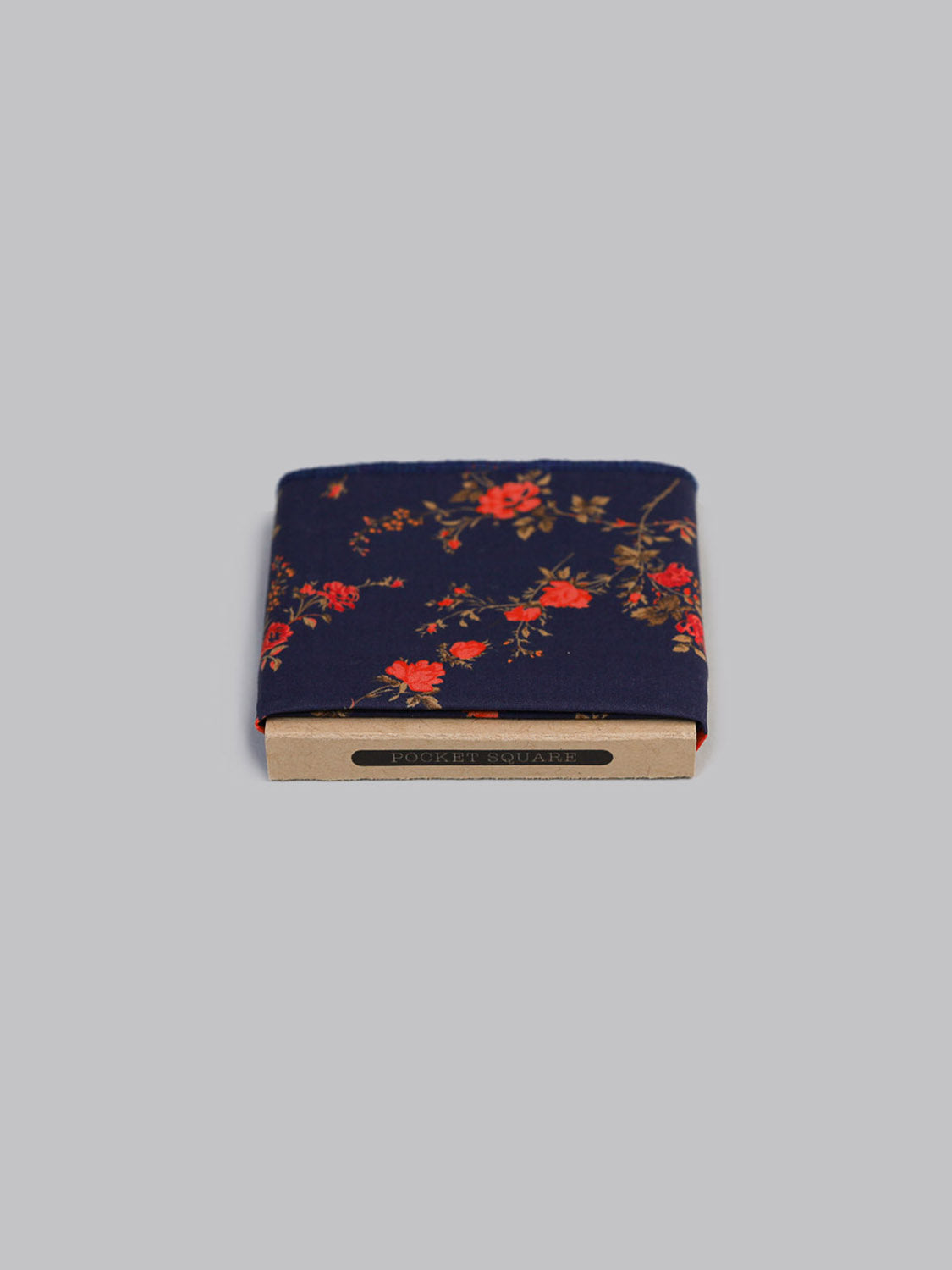 The Liberty™ Elizabeth Pocket Square by ID Menswear features a folded navy blue Tana Lawn cotton with red and orange florals, neatly packaged in a cardboard holder and displayed against a plain light gray background.