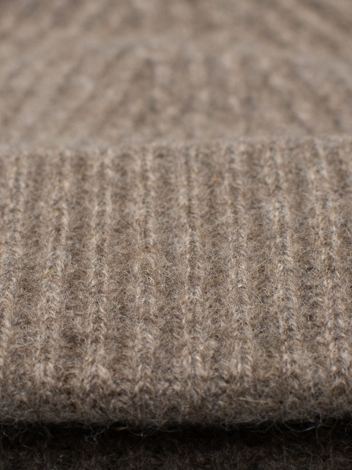 Close-up of the Everest Cashmere Beanie by ID Menswear, crafted from light brown, ribbed-knit woolen fabric. Its soft texture and vertical ridges offer versatile style as a lightweight accessory.