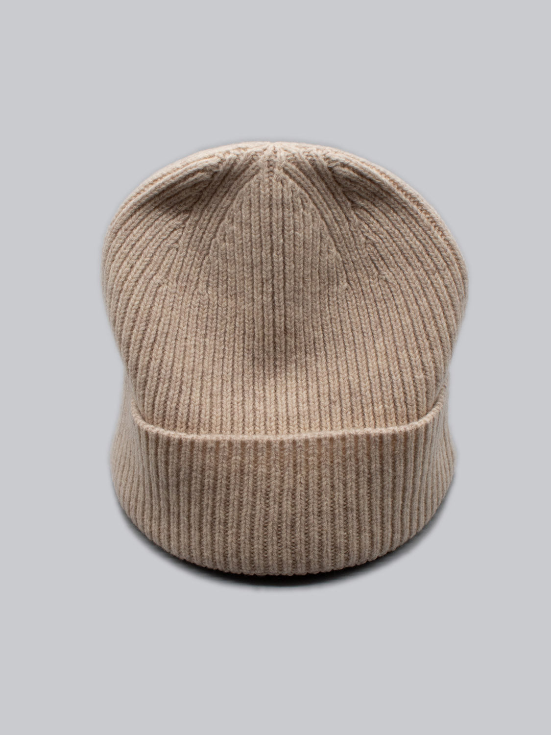 The Fuji Merino Wool Beanie by ID Menswear, made from 100% Merino wool, is your perfect winter companion. It features a beige ribbed knit design and sits against a gray background.