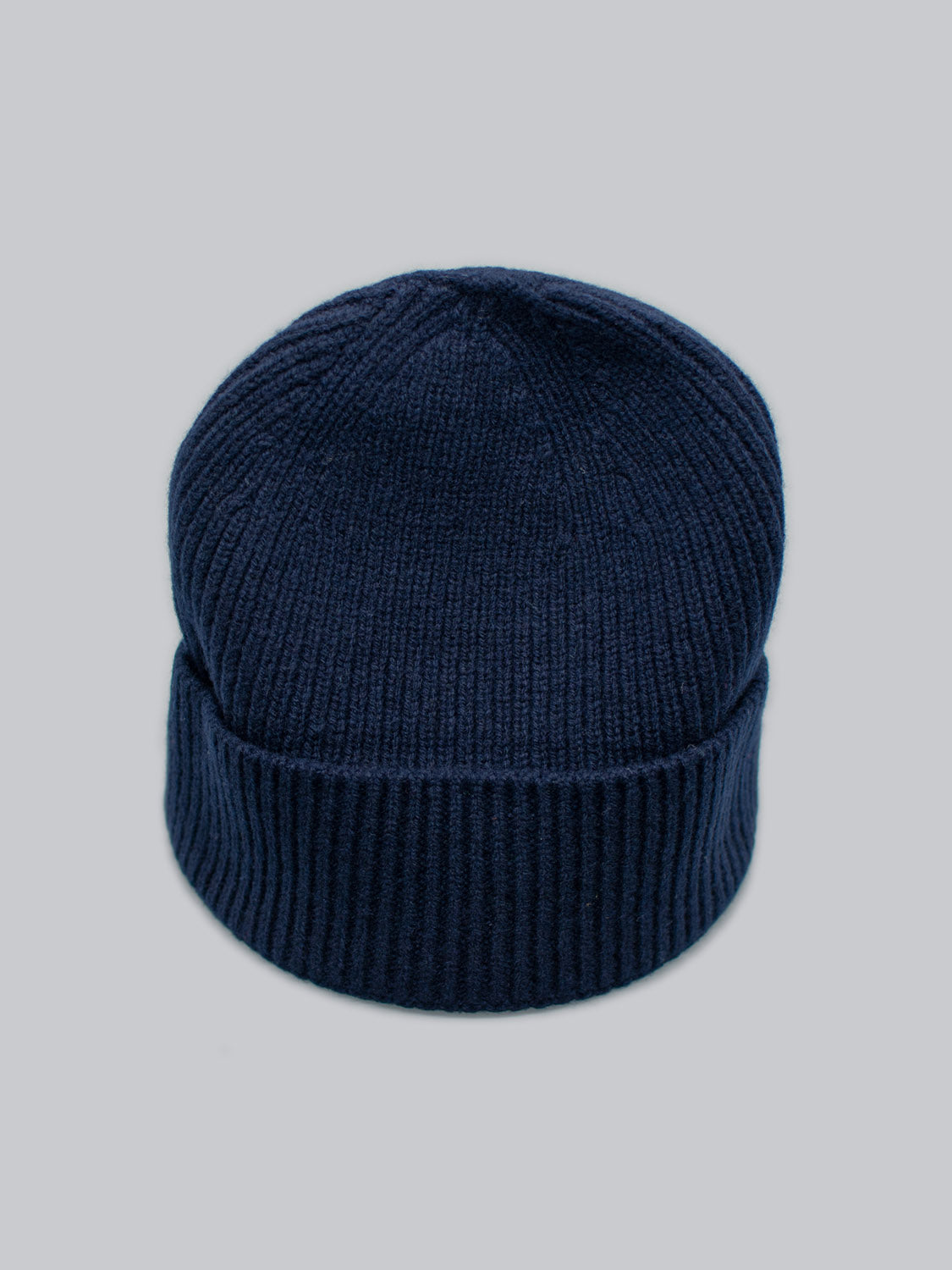A dark blue Fuji Merino Wool Beanie from ID Menswear, featuring a folded brim, is showcased on a plain gray background.