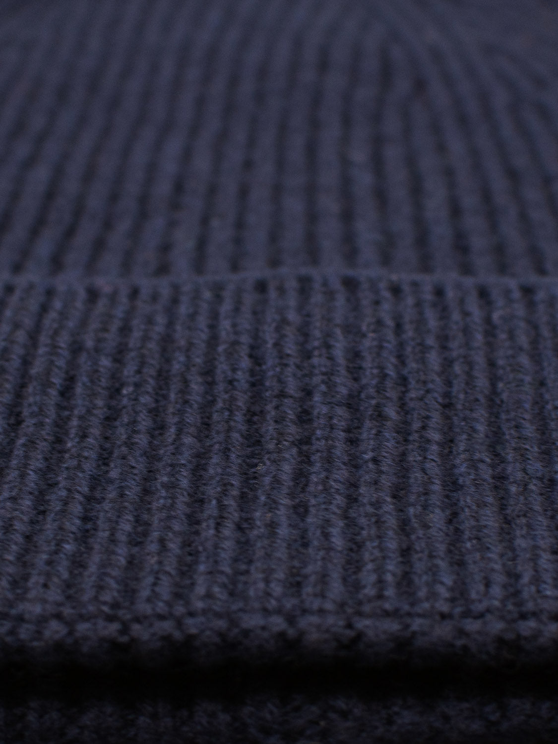 Close-up of the dark gray Fuji Merino Wool Beanie by ID Menswear, showcasing its ribbed knit fabric. The inviting texture and horizontal seam in the upper third highlight its softness, making it perfect for cozy winter wear.