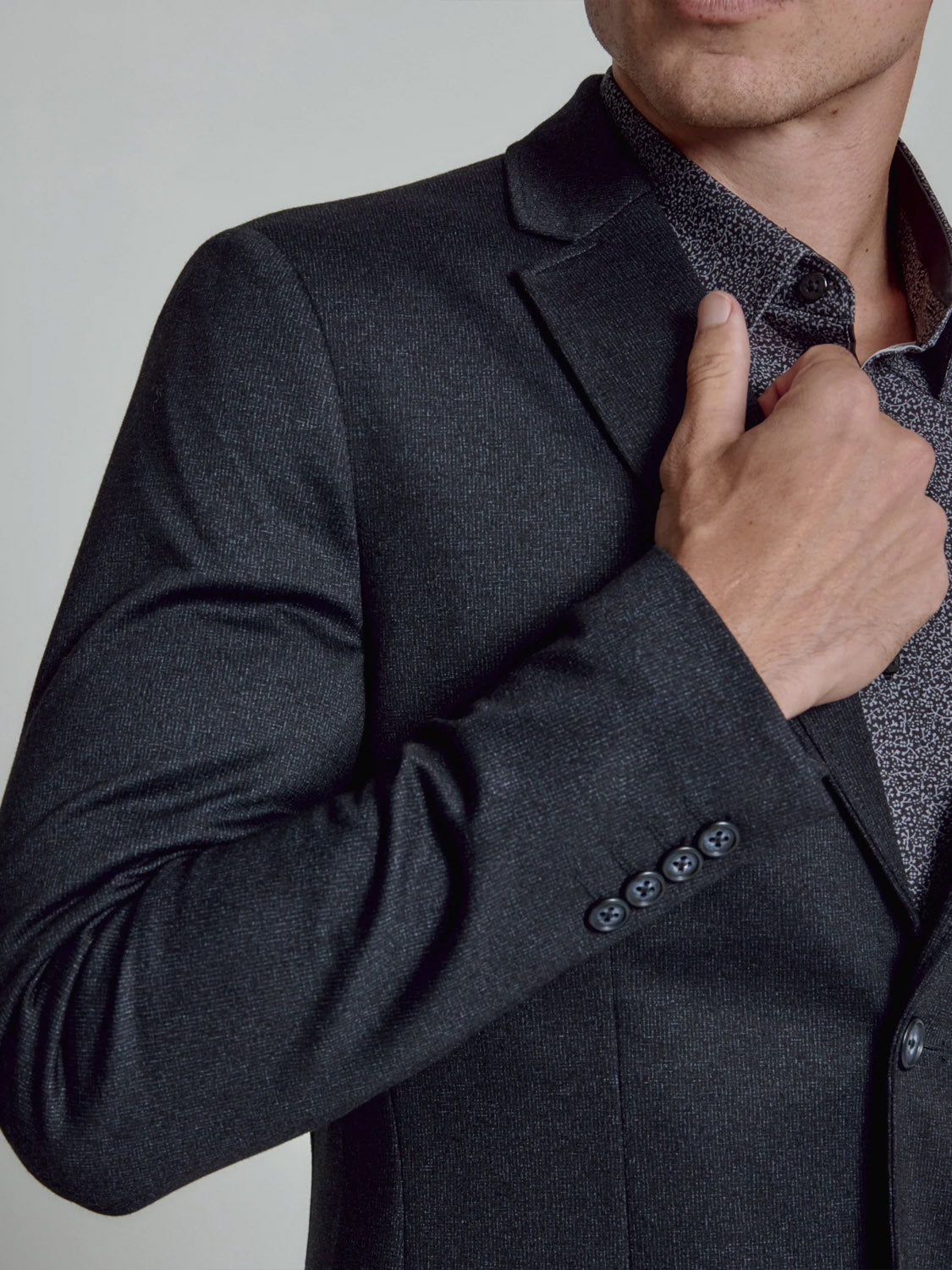 A man adjusts his 7 Diamonds Gatsby Blazer, featuring a notched lapel, paired with a patterned shirt. The photo, cropped to his lower face and upper body, highlights the blazer's refined, dressy style.