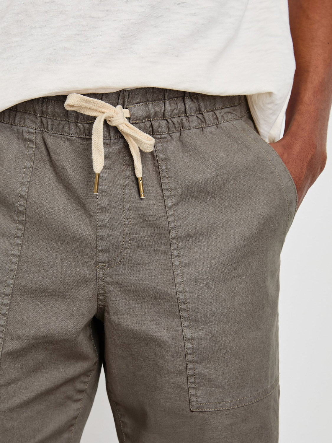 Confidently striking a pose, the individual wears the Rails Gobi Pant in slim fit olive green with a beige tie, hand in pocket. The slight glimpse of a white shirt adds a touch of casual elegance.