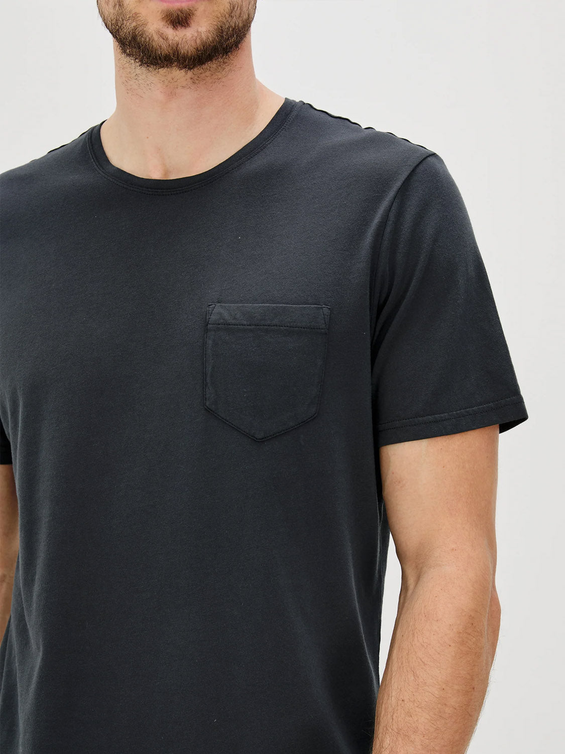 A person wears the Rails Johnny T-Shirt—a plain black soft cotton jersey with short sleeves and a chest pocket—shown from shoulders to waist against a light background, head partially out of frame.