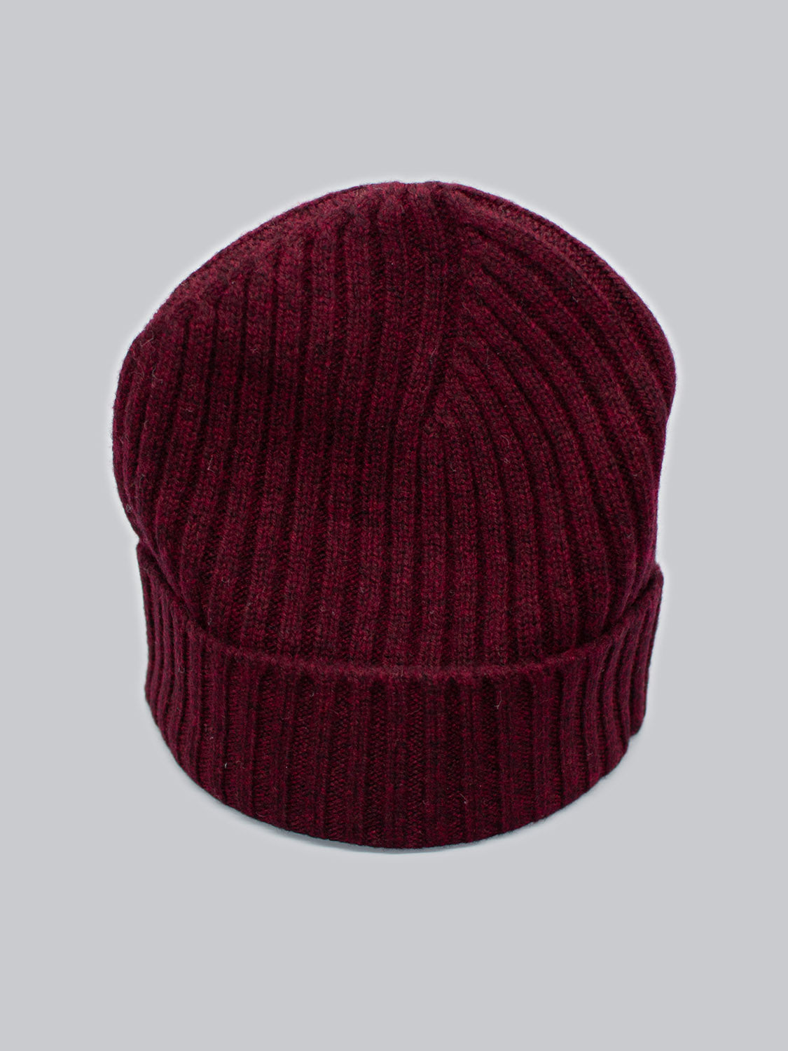 The Kailash Merino Wool Beanie by ID Menswear, in dark red ribbed knit, is captured against a light gray backdrop, offering warmth and softness for outdoor adventures.