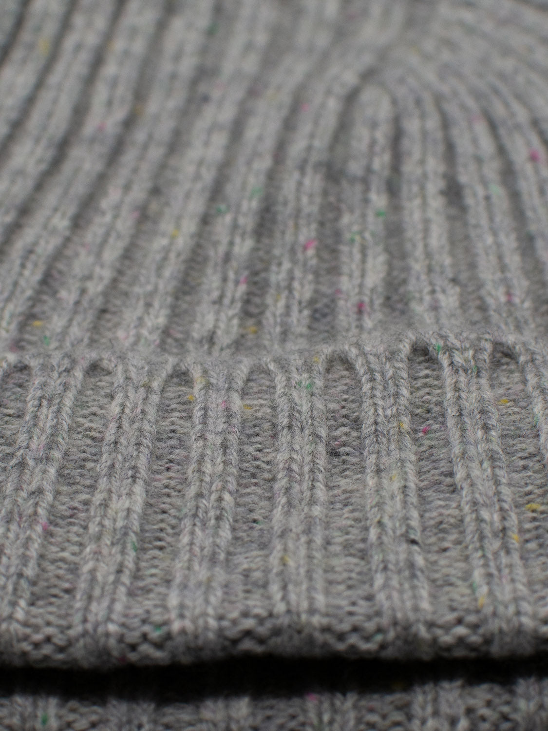 A close-up of the gray ribbed texture with subtle multicolored speckles of the Kailash Merino Wool Beanie by ID Menswear evokes warmth and softness, perfect for outdoor adventures.