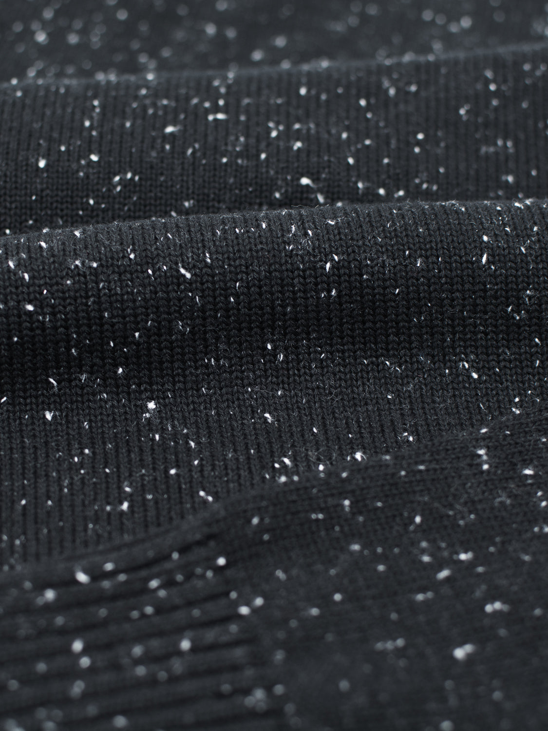 Close-up of the Malmo Speckled Cotton Sweater by ID Menswear, featuring a dark fabric with white speckles and a plain knit design similar to a cozy crew neck. The slightly ribbed material hints at its warmth and comfort.