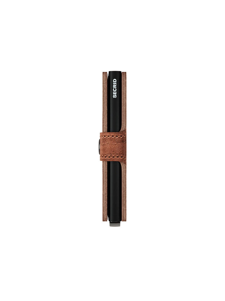 A side view of the Secrid Miniwallet Dutch Martin in brown leather with a strap shows the edge of a black RFID card protector labeled SECRID in white text against a white background.