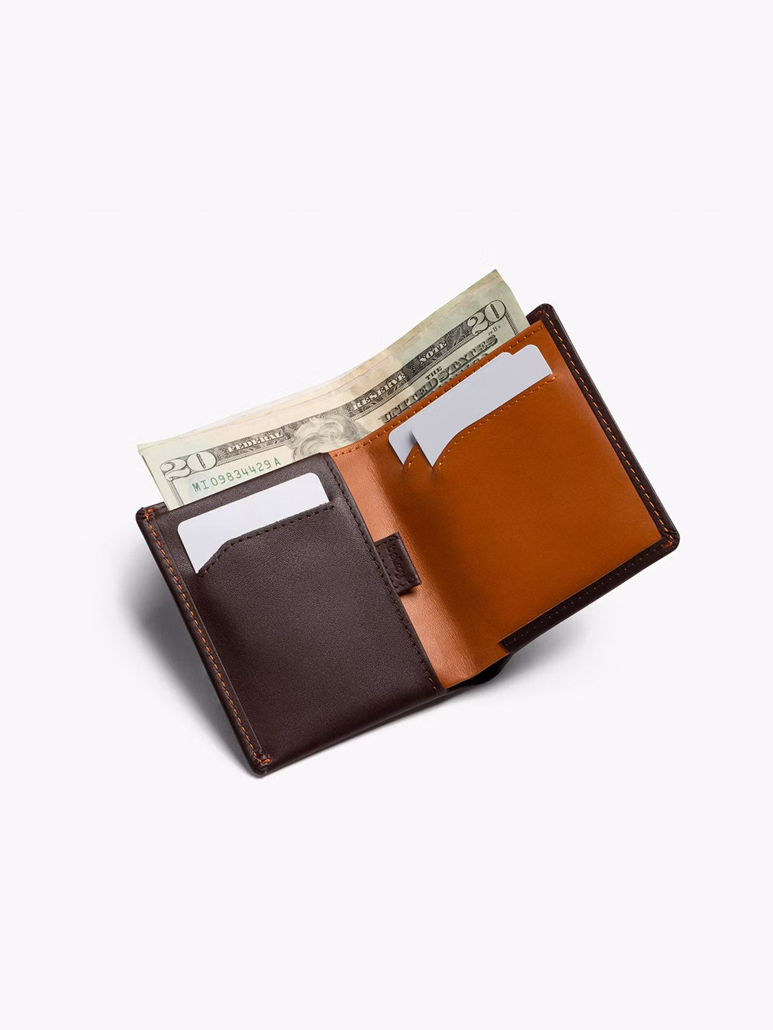 The Bellroy Note Sleeve Wallet, shown in brown and tan leather with two white cards and a folded twenty-dollar bill, is displayed on a light background—ideal as a travel billfold.