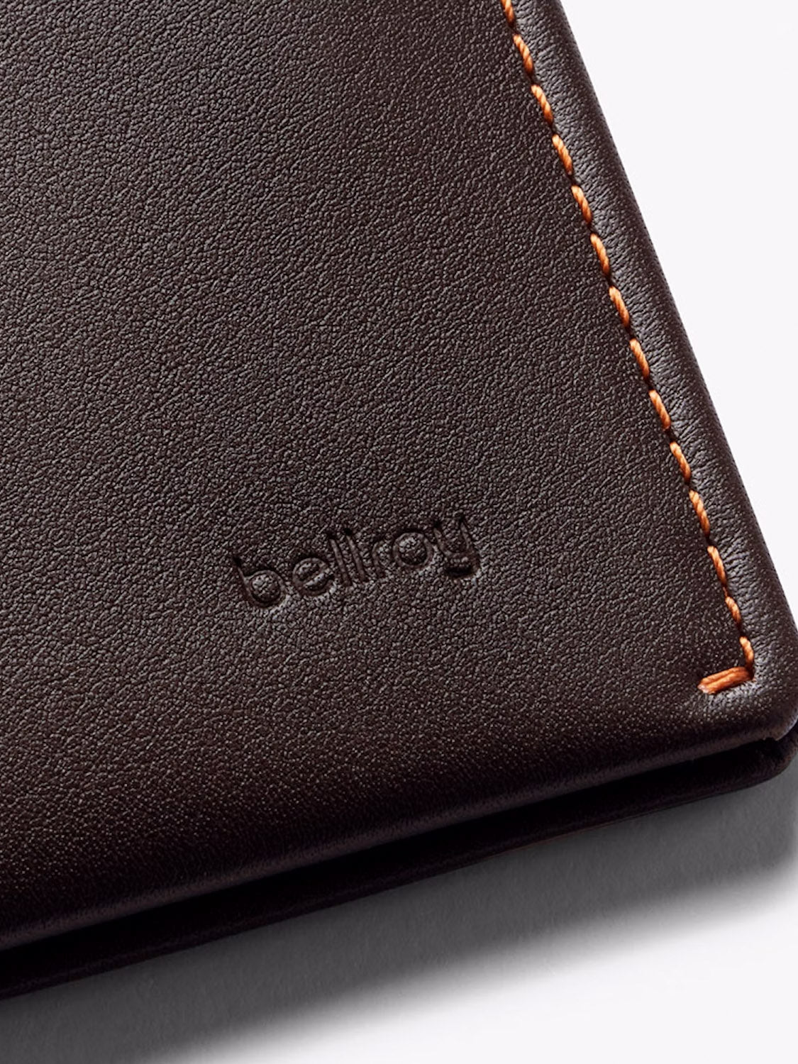 Close-up of the Bellroy Note Sleeve Wallet, a dark brown leather slim billfold featuring orange edge stitching and "bellroy" embossed on its surface.