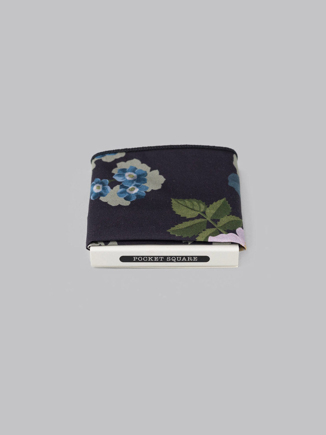 The ID Menswear Liberty™ Nysa Pocket Square, in navy blue with a blue and green floral pattern, is neatly folded in a white holder labeled Pocket Square and shown against a plain gray background.