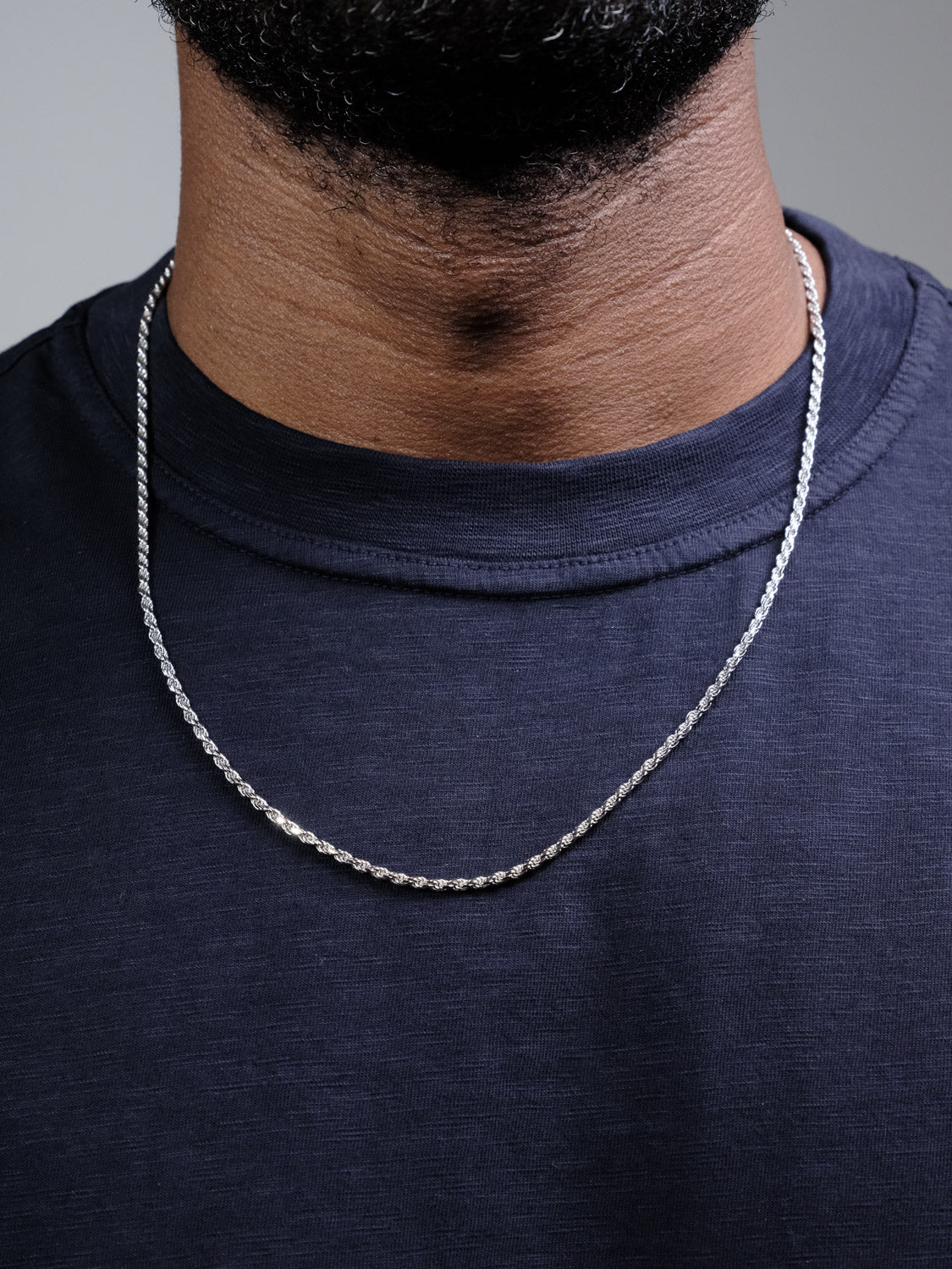 A close-up of a person wearing the Orion 50 Rope Chain Necklace by ID Menswear over a dark navy blue t-shirt. Only the lower half of the face and neck are visible, showcasing the elegant Italian-made sterling silver design.