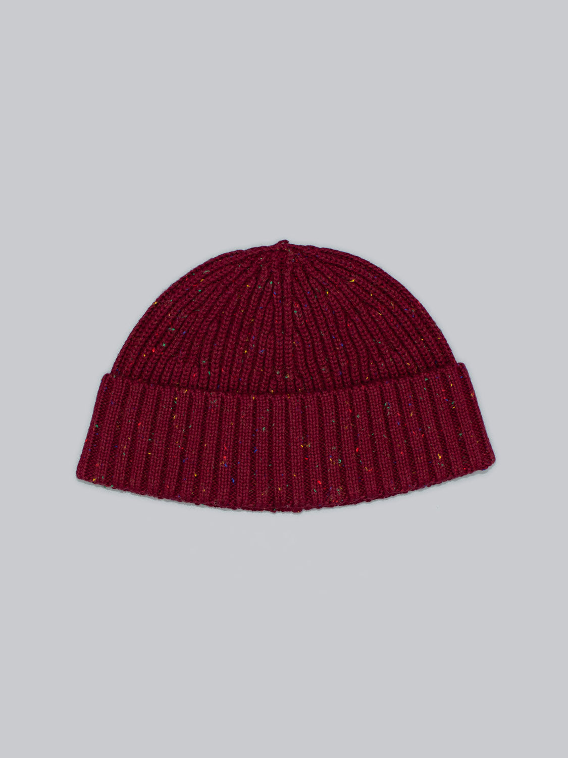 ID Menswears Paro Speckled Cotton Fishermans Beanie features a maroon hue with a classic folded brim and ribbed texture. Made from speckled yarn, it displays multicolored speckles on a plain gray background.