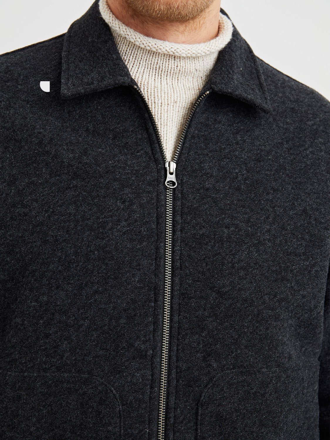 A person wears the Shael Jacket by Rails in dark grey over a light beige ribbed turtleneck sweater, shown from shoulders to upper chest against a plain background.