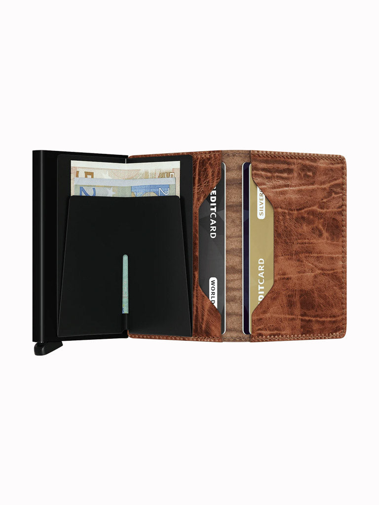 The Secrid Slimwallet Dutch Martin in brown leather features RFID protection and a black metal case, holding euro banknotes and several CREDITCARD and CURRENCY cards, displayed open on a white background.