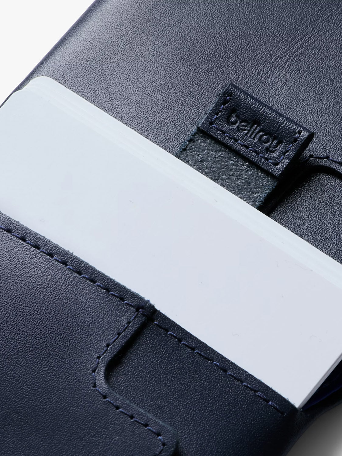 A close-up of the Bellroy Slim Sleeve Wallet shows its neat stitching, a white card in the outer slot, and a small leather tag embossed with the brand name.