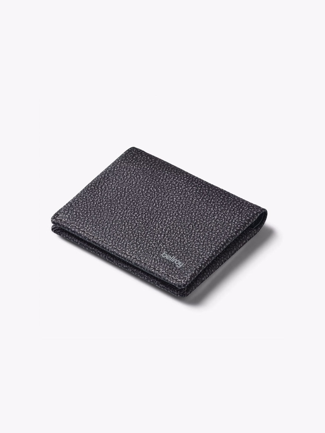 A closed Bellroy Slim Sleeve Wallet in black textured leather rests on a plain light gray background, showcasing its minimalist design, subtle stitching, and a small embossed logo on the lower right corner.